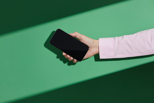 A woman's hand holding blank screen mobile phone over green background
