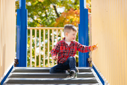 Young boy sitting happily on stairs of playground equipment. 