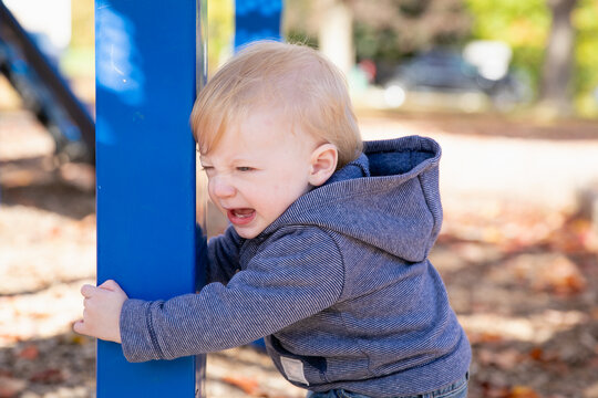 Toddler child at a playground holding on to a post and crying angrily