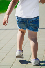 Rear view of a little child girl in summer clothes walking alone in green park.