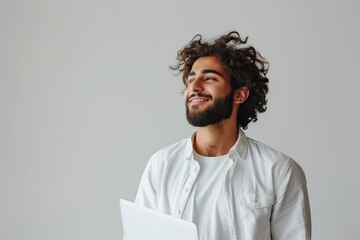 Obraz premium A man with a beard and a white shirt is smiling and holding a laptop. Concept of happiness and contentment, as the man is enjoying his time with the laptop