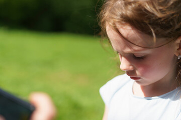 A sad little cute preschooler girl in a green clearing in the forest looks down when she is...