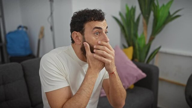 Handsome middle age man, shocked and covering mouth with hand at home -a secret mistake revealed in understandable astonishment