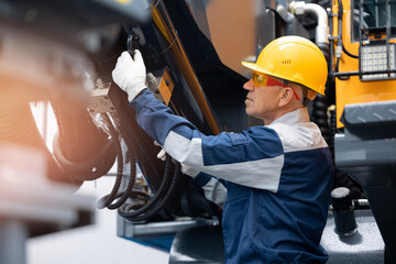 Mechanic repairing hydraulic hose in drilling machine, exploration drilling. Adult man in hard hat...