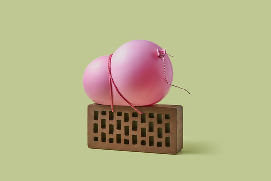 Pink balloon tied with thread to brick over green background