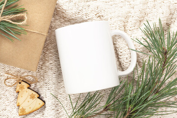 Christmas mockup of white mug on knitted plaid with gift box, tree branch and decorations. Blank coffee cup mug mock up, flat lay.