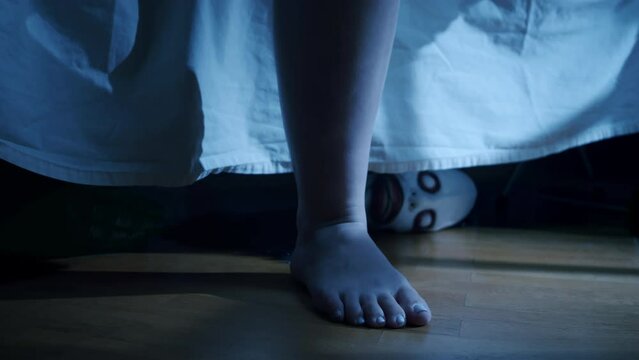 Scary monster face under bed want to grabbing teen girl by legs, close up. Creepy hand want to catch girl. Suspense horror concept. Halloween nightmare
