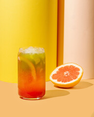 Colorful refreshing citrus beverage with ice in a glass, perfect for summer celebrations or beach parties, against vibrant yellow background