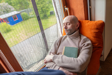 Young man relaxing with book on windowsill in old house, reclining on windowsill, self-reflection,...
