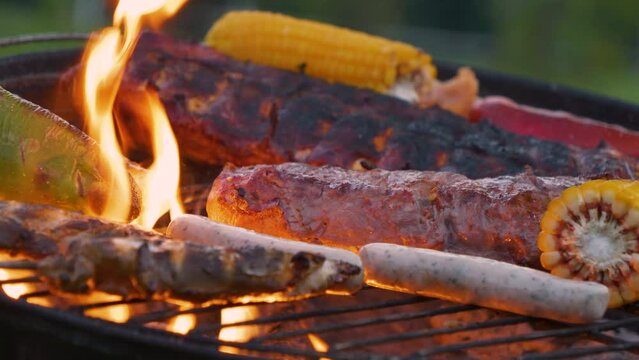 CLOSE UP: Barbecue grill loaded with a variety of roasted meats and vegetables. Mouthwatering selection of delicious food is being grilled outside at a BBQ party in the garden during summer holidays.