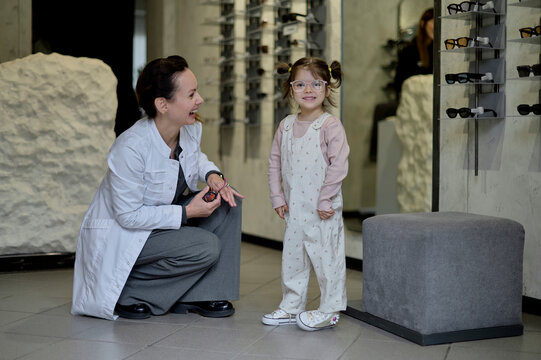 A female optician selects glasses for a girl