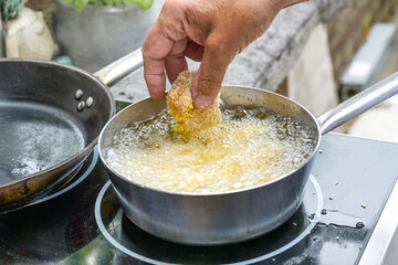 Hand putting a piece of panko breaded chicken into a pot with hot boiling oil for deep frying, cooking in an outdoor kitchen, selected focus