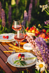 Romantic surprise, marriage proposal. Elegant decoration. Private wedding party for two, table set with floral decor, chandelier, fruits, wine in field or meadow. Summer, sunset, golden hour