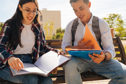 Happy students studying on bench in campus