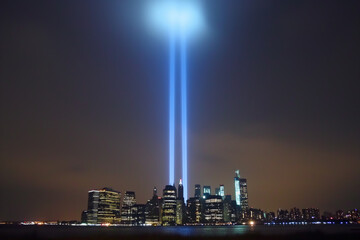 Obraz premium A city skyline at night, distinguished by two beams of light emanating from the summit of a skyscraper, piercing darkness and forming an iconic tower silhouette.Suitable for Patriot Day,Memorial Day