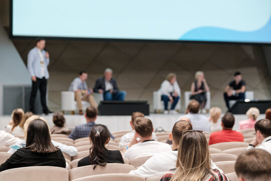 Tech conference featuring speakers on stage discussing various topics while the audience listens attentively. Modern venue with professional atmosphere.