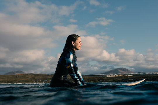 A happy young surfer admires a sunset floating on her surfboard