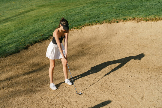  young woman playing golf in the sun, her ball is a trap/ bun 