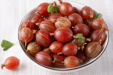 Fresh, sweet red gooseberries in a white cup on a white background.