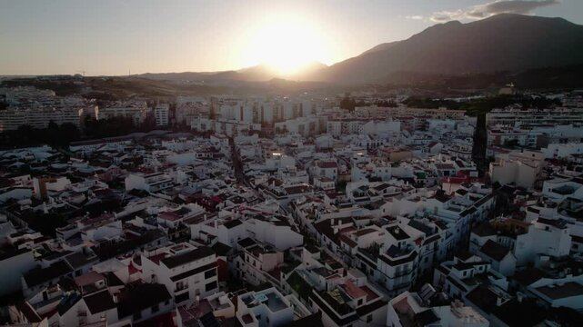 Aerial cityscape at sunset with a mountain in the background, creating a warm glow in the sky
