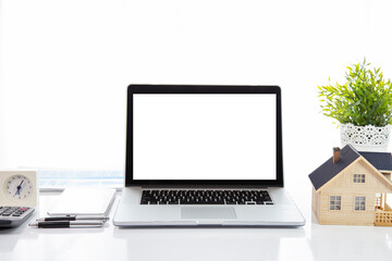 A laptop with a white screen on the table with a house model and a clock