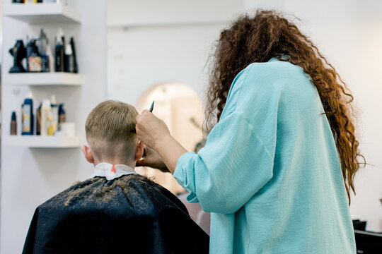 A little fair-haired boy is getting his hair cut in a barber shop.  