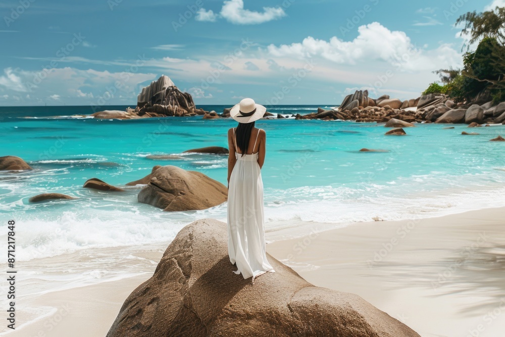 Poster a person standing on top of a large rock formation on a beach, with the ocean and sky in the backgro