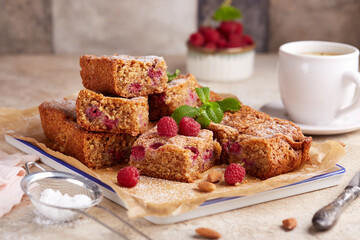 Almond sponge cake bars with raspberries, covered with sugar powder. Delicious homemade sweet pie bars with seasonal berries. 