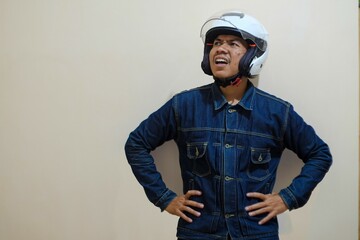 A Southeast Asian man wearing a denim jacket and white motorcycle helmet on his head and tired face, showing tired.