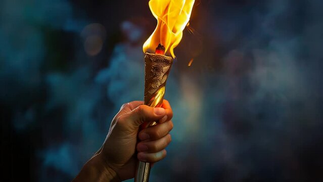 Hand holding burning torch in slow motion against dark backdrop for sports events or motivational video themes