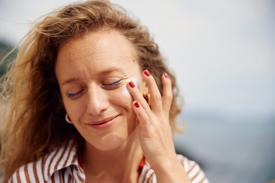 Curly woman applies cream to her face