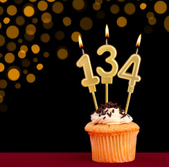 Number 134 birthday candle - Cupcake on black background with out of focus lights
