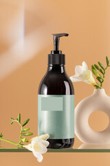 Cosmetic dispenser bottle and fresh freesias on orange