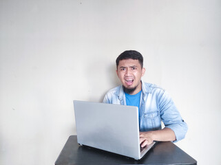 Adult Asian man sitting in front of his laptop showing shocked face expression