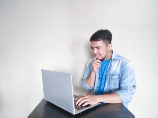 Asian mature man is thinking something while working in front of his laptop
