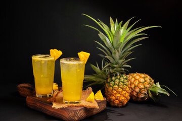Pineapple juice with fresh pineapple from the garden Healthy summer food, cocktails, natural drinks Green leaves. Isolated on black background.