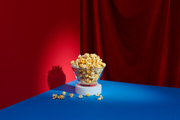 Bucket of popcorn on red table over blue curtain background