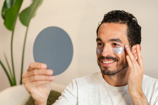 A man with a beard and mustache applying patches under his eyes
