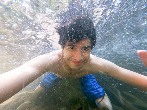 Underwater self-portrait of a smiling young man in bermuda shorts