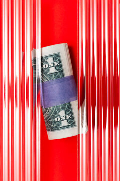One dollar banknote roll on red background under corrugated glass