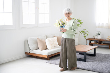 部屋で花を持つシニア女性　趣味の園芸やお花