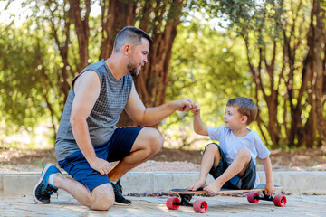 A Brazilian father playing with his young son on the street. The son sits on a skateboard, and they bump fists, sharing a casual and playful moment together on Father's Day