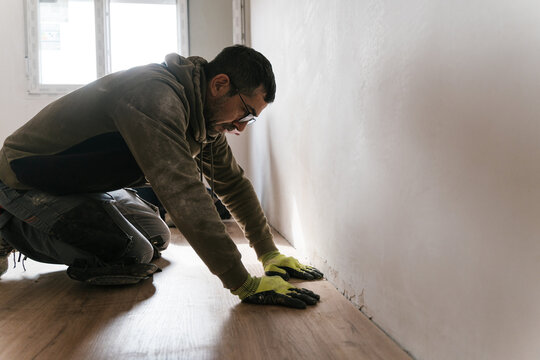 Male worker installing wooden floor in apartment