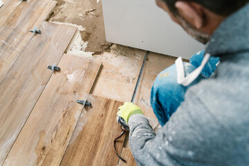 Crop workman measuring floor while installing wooden tiles in house