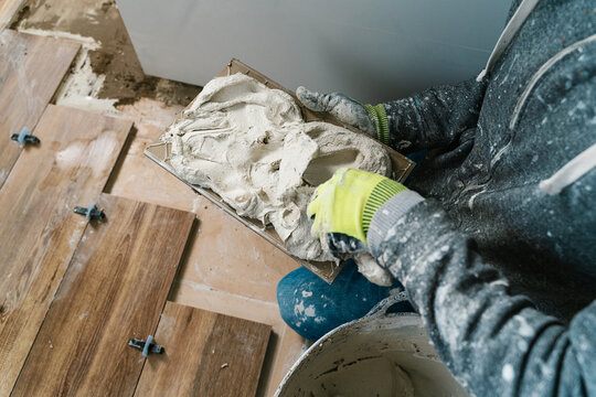 Anonymous workman installing wooden flooring with tile adhesive