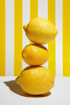 Three lemons piled on yellow striped white background in sunlight. 