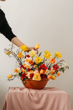 Woman adding tulip to spring flower arrangement in a vase