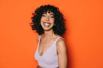 Smiling woman with curly hair against bright orange background