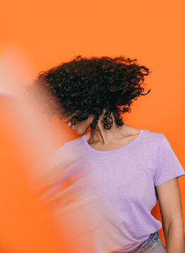 Woman with curly hair in lilac top against vibrant orange background