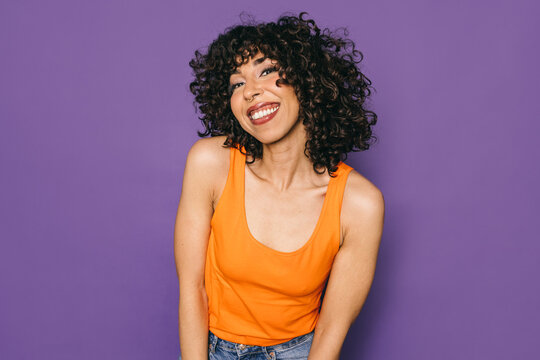 Joyful Moroccan woman in orange top against purple background
